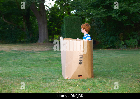 Ragazzo giovane guardando dalla scatola di cartone in giardino Foto Stock