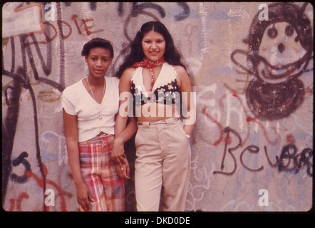 Due ragazze latine posano di fronte a una vivace parete di graffiti a Lynch Park, Brooklyn. Questo progetto di arte urbana riflette l'intersezione tra cultura e Street art nella comunità, sottolineando l'espressione dell'identità attraverso l'arte pubblica. Foto Stock