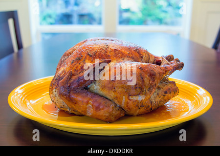 Cotto intero il tacchino arrosto sul piatto giallo seduto a tavola per la cena di ringraziamento Foto Stock