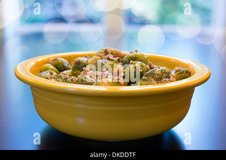 I cavoletti di Bruxelles cotti con pancetta Olio d'oliva e cipolla nel recipiente di colore giallo con Bokeh sfondo sfocato Foto Stock