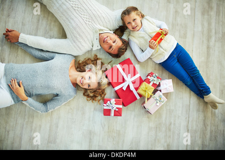 La famiglia felice con giftboxes sdraiato sul pavimento e guardando la fotocamera Foto Stock