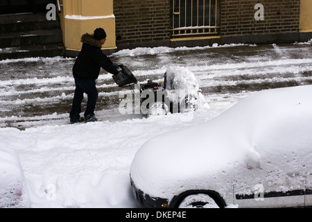 L'uomo operando un spalaneve per cancellare il marciapiede dopo una tempesta di neve Foto Stock