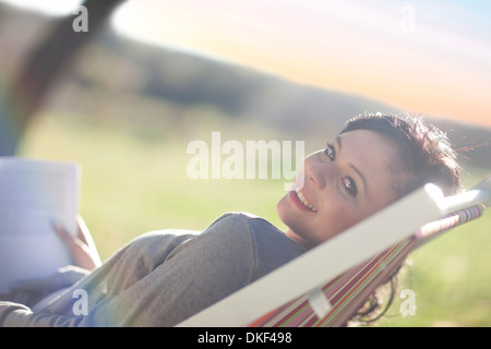 Giovane donna reclinata in sedia a sdraio con libro Foto Stock