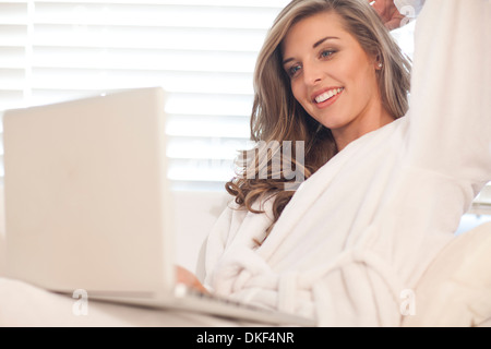 Giovane donna giaceva a letto con il computer portatile Foto Stock
