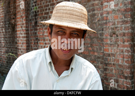 Colorate in rosso di betel dado grin su una bicicletta di Yangon taxi driver indossando un cappello di paglia contro un muro di mattoni del Myanmar (Birmania) Foto Stock