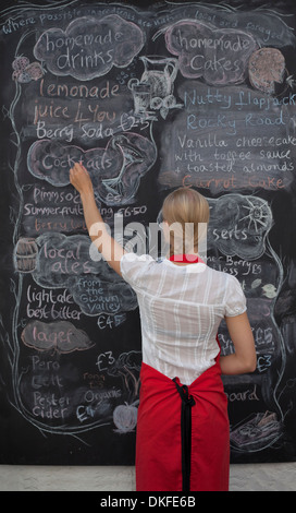 Cameriera di scrivere sulla lavagna menu in cafe Foto Stock