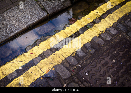 Doppie linee di colore giallo su fondo bagnato acciottolato nel nord di Londra, Inghilterra. Foto Stock