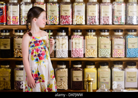 Ragazza in piedi nel negozio di dolci nella parte anteriore degli scaffali di prodotti a base di zuccheri Foto Stock