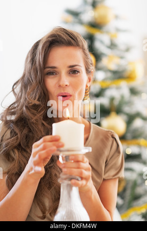 Giovane donna soffiando candela nella parte anteriore dell albero di natale Foto Stock