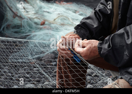 Fisherman riparazione rete sulla spiaggia ghiaiosa Foto Stock