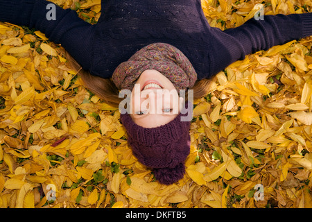 Giovane donna giacente in foglie di autunno Foto Stock