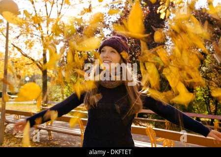 Giovane donna gettando su foglie di autunno nel parco Foto Stock