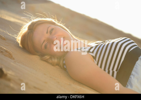 Giovane donna che indossa abiti che giace sulla spiaggia Foto Stock