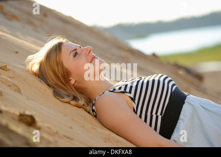 Giovane donna che indossa abiti che giace sulla spiaggia Foto Stock