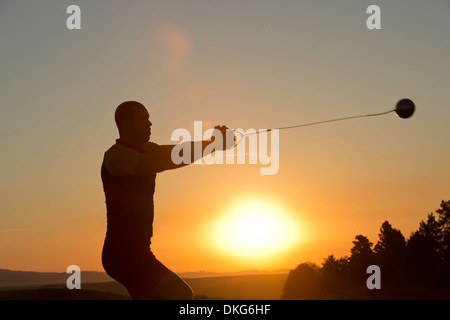 Giovane uomo si prepara a lanciare il martello al tramonto Foto Stock