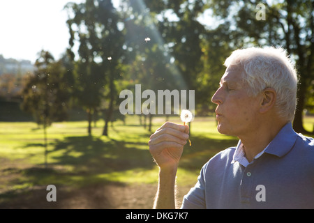 Senior uomo soffiando tarassaco orologio Foto Stock