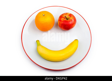 Tre diversi pezzi di frutta che compongono un volto sorridente su una piastra su uno sfondo bianco. Foto Stock