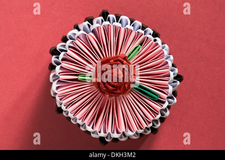 Guardando verso il basso su origami cupcake al cioccolato con Red Rose fiore sulla cima isolata su sfondo rosso Foto Stock