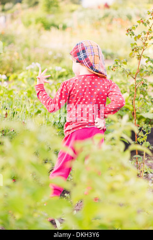 Vista posteriore del bambino in piedi in giardino a studiare la sua mano Foto Stock