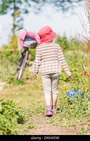 Vista posteriore di un giovane bambino esplorando la natura, la visione di piante verdi e fiori Foto Stock