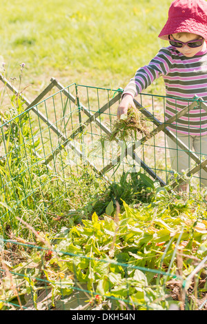 Vista frontale di un giovane bambino in giardino contribuendo con faccende. Il riempimento del compost bin con piante e fiori. Foto Stock