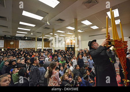 Un ortodosso rabbino ebreo luci Hanukkah candele come studenti e congregants guarda al Lubavitch sede a Brooklyn, NY Foto Stock