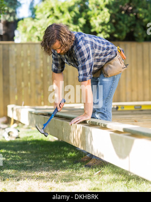 Lavoratore utilizzando un martello sul telaio di legno al sito in costruzione Foto Stock