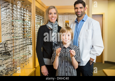 Ragazzo tenendo i bicchieri con la madre e ottico in negozio Foto Stock