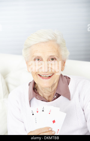 Sorridente donna senior azienda quattro assi in mano mentre le carte da gioco Foto Stock