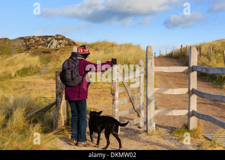 Donna walker a piedi un cane baciare apertura cancello sul percorso principale su Ynys Llanddwyn Island. Newborough Isola di Anglesey North Wales UK Foto Stock