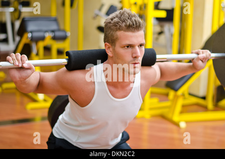 Bel giovane facendo squat in palestra con barbell Foto Stock