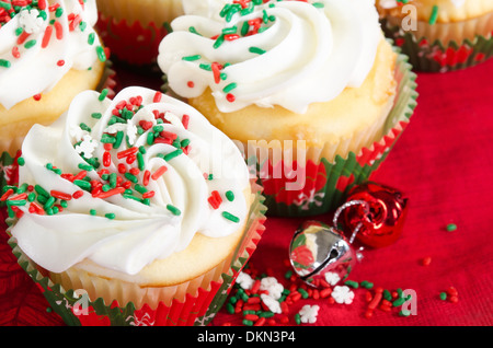 Holiday tortine con glassa alla vaniglia e il rosso e il verde spruzza. Rosso sfondo per le vacanze di Natale campane. Foto Stock