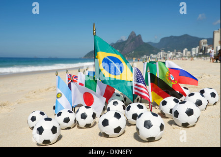 Il team internazionale di bandiere del mondo con palloni da calcio sulla spiaggia di Rio de Janeiro Foto Stock