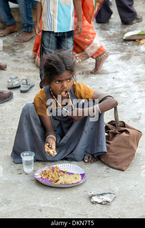 Povero indiano di casta inferiore ragazza di mangiare cibo gratuito su un indiano street, durante un festival. Andhra Pradesh, India Foto Stock