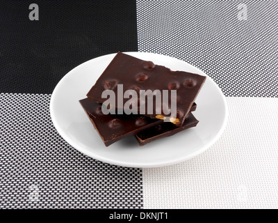 Spaccate parti di cioccolato in piastra bianca Foto Stock