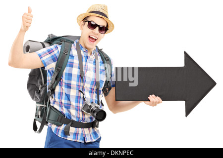 Turistico con zaino tenendo una grande freccia nera e dando pollice in alto Foto Stock