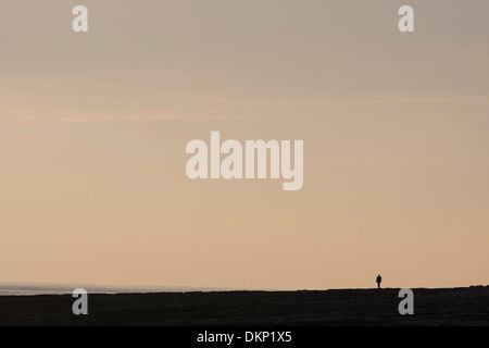 Distante lone figura minuscola sulla spiaggia al tramonto Foto Stock