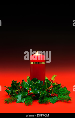 Un rosso christmas candle con holly, edera e abete rosso su rosso sfondo graduata. Copia spazio per aggiungere il proprio messaggio. Foto Stock