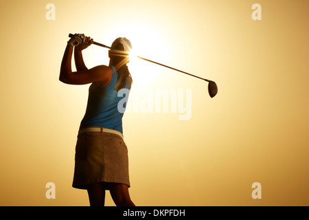 Sole che splende dietro donna swinging golf club Foto Stock