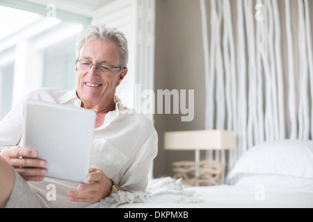 Uomo anziano con tavoletta digitale sul letto Foto Stock