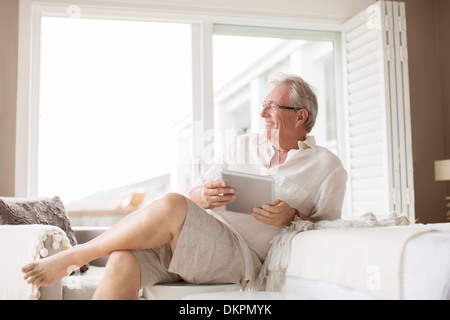 Uomo anziano con tavoletta digitale in camera da letto Foto Stock