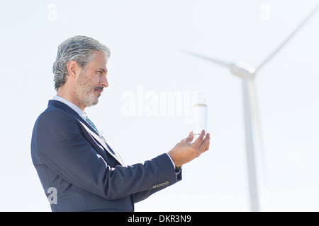 Imprenditore esaminando un bicchiere di acqua mediante la turbina eolica Foto Stock