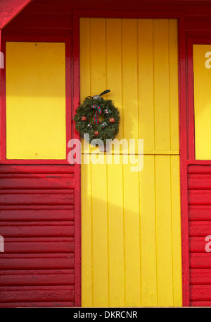 Ghirlanda di festosa appeso sulla porta di un colore giallo brillante e red beach hut a Swanage in Dicembre Foto Stock