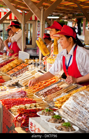 Le ragazze di vendita alimentari presso la famosa Wangfujing Street, il mercato notturno, Pechino, Repubblica Popolare Cinese, in Asia Foto Stock