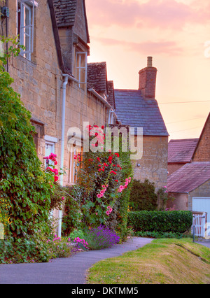 Cotswold cottage con hollyhocks e le rose al tramonto, Mickleton vicino a Chipping Campden, Gloucestershire, Inghilterra. Foto Stock