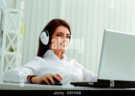 Giovane imprenditrice nelle cuffie al lavoro su un notebook in ufficio Foto Stock