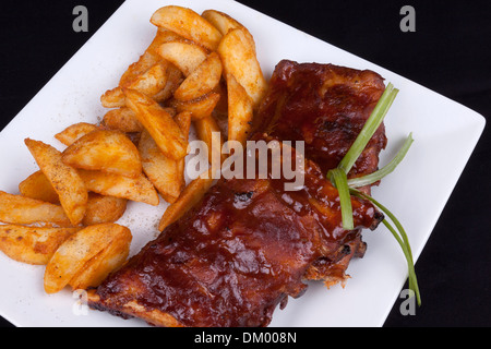 BBQ Ribs con spicchi di patate su una piastra bianca. Foto Stock