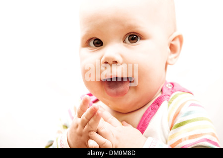 Funny little brown eyed Caucasian baby che mostra la linguetta Foto Stock