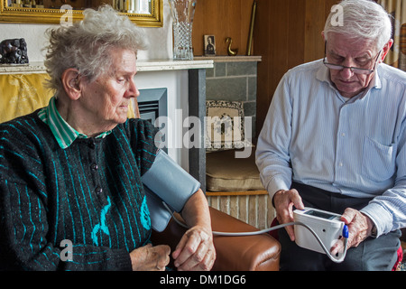 In prossimità della coppia di anziani controllare il proprio sangue-pressione utilizzando un digital monitor della pressione del sangue nel salotto di casa Foto Stock