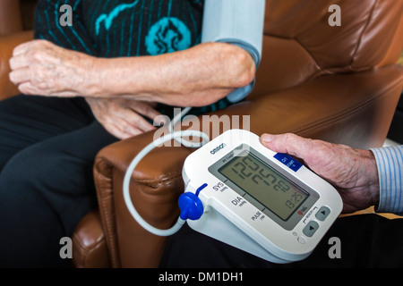 In prossimità della coppia di anziani controllare il proprio sangue-pressione utilizzando un digital monitor della pressione del sangue nel salotto di casa Foto Stock